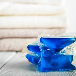 Blue laundry detergent pods stacked on white surface with folded towels behind