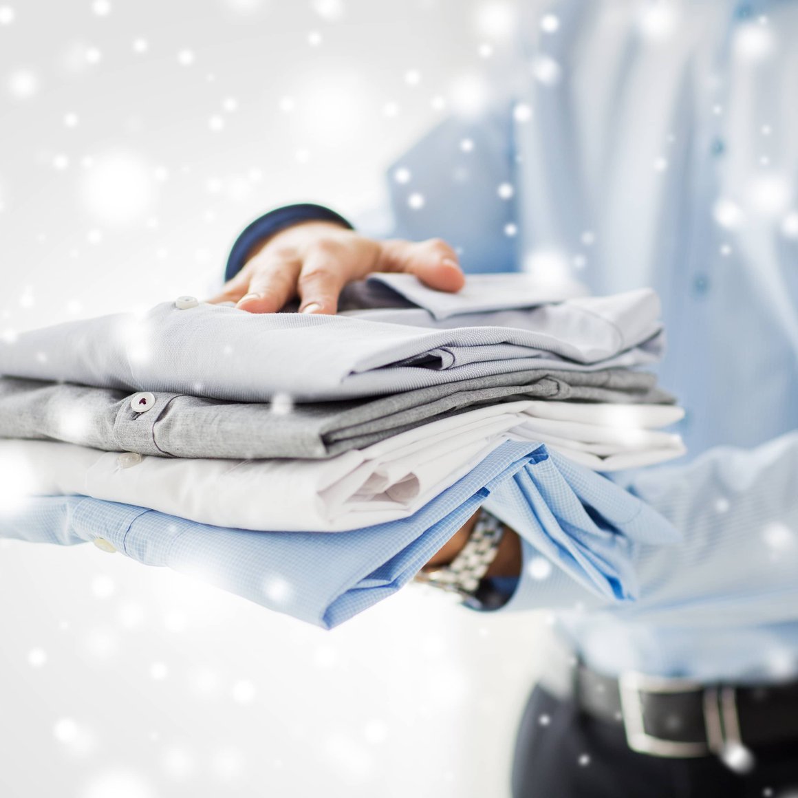 Person holding neatly folded stack of clean clothes with winter snowflake background
